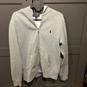 Grå hoodie från Polo Ralph Lauren - Riktigt snygg polo zip. Storlek 14-16 år. Fint skick inga skador. Köpt på kidz brand store. 