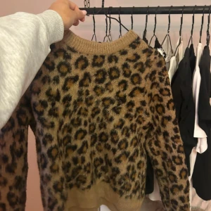 Leopardmönstrad stickad tröja  - Säljer en fluffig stickad tröja från HM i storlek XS med leopardmönster i bruna och svarta toner. Tröjan har rund hals och långa ärmar, perfekt för dig som vill ha en cool och trendig look. Materialet är mjukt och ger en skön känsla.