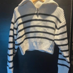Randig croppad stickad tröja Gina Tricot - Superfin croppad stickad tröja från Gina Tricot i vit med svarta ränder. Tröjan har en bred krage med half zip-dragkedja och ribbade muddar. Perfekt för dig som gillar en chill och trendig look med långärmad passform.