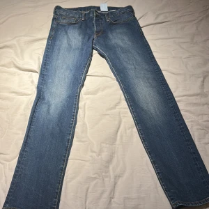 Blå raka jeans med klassisk tvätt - Snygga blå jeans med klassisk tvätt och raka ben. Jeansen har fem fickor, normal passform och subtila slitningar framtill. Perfekta för en avslappnad stil och passar till det mesta. Tidlös modell med bekväm midja.