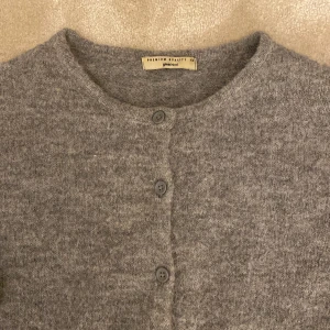 Grå stickad kofta från Gina Tricot - Mysig grå stickad kofta från Gina Tricot med rund halsringning och knappar framtill. Koftan har lång ärm och är i en mjuk ullblandning som passar perfekt till kyliga dagar. Enkel och stilren design som är lätt att matcha.