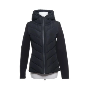 Svart pufferjacka med huva från Zara - Svart pufferjacka från Zara med snyggt chevronmönster på kroppen och släta ärmar. Jackan har en stor huva och dragkedja framtill. Materialet är polyester och jackan har en normal passform, perfekt för kyliga dagar.