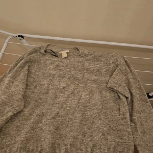 Beige stickad tröja från H&M - Mysig beige stickad tröja från H&M i storlek S. Tröjan har en rund halsringning och långa ärmar med ribbade muddar vid ärmslut och nederkant. Perfekt för att hålla värmen under kyliga dagar.