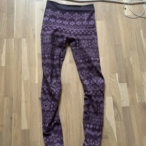 Lila leggings med vintermönster - Mysiga lila leggings med vinterinspirerat mönster av snöflingor, hjärtan och geometriska former. Insidan är mjukt fleecefodrad för extra värme. Perfekta för kalla dagar när du vill vara både bekväm och snygg.