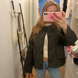 Quiltad mörkgrön jacka från Zara - Säljer en quiltad mörkgrön jacka från Zara. Jackan har stora fickor framtill, knäppning med både knapp och snörning samt rundad halsringning. Perfekt för lager-på-lager och chill stil.