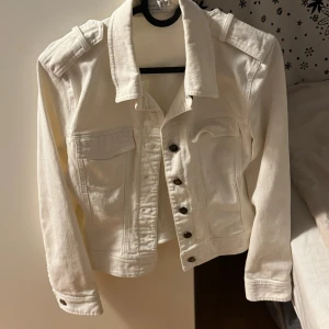 Vit jeansjacka från hennes collection , strl 36 - Snygg vit jeansjacka från hennes collection i storlek 36. Jackan har klassisk krage, långa ärmar, axelklaffar och coola metallknappar framtill. Två bröstfickor med lock och en croppad passform som ger en fräsch vibe. Perfekt för dig som gillar stilrena och enkla plagg.