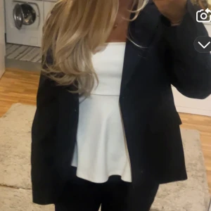 Vit bandeau tubtopp med volang - Säljer en vit bandeau tubtopp med snygg volang nedtill. Toppen är axelbandslös och har en figurnära passform upptill som går ut i en luftig peplum. Perfekt för dig som vill ha en clean och fräsch look med lite extra edge.