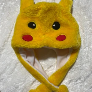 Gul Pikachu mössa med öron - Supermysig gul Pikachu mössa med söta öron och broderade ansiktsdetaljer. Tillverkad i mjuk pälsliknande syntetmaterial, perfekt för dig som älskar Pokémon och vill sticka ut med en rolig huvudbonad.