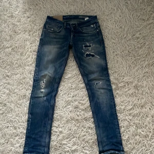 Dondup George skinny jeans blå - Snygga blå skinny jeans från Dondup, modell George. Jeansen har slitna detaljer och hål på framsidan för en cool, edgy look. Klassisk femficksdesign, låg midja och smal passform. Materialet är jeans med lätt stretch för extra komfort.