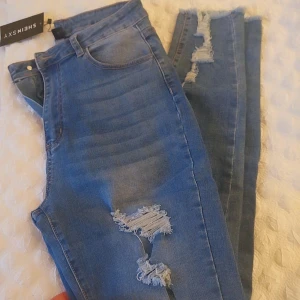 Blå ripped jeans från SHEIN SXY - Snygga blå jeans från SHEIN SXY med flera slitningar och ripped detaljer längs benen. Modellen har klassisk femficksdesign, hög midja och raka ben. Jeansen är tillverkade i stretchigt denim för skön passform och cool look.
