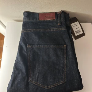 Jeans från Oscar Jacobson - Snygga oanvända mörkblå jeans från Oscar Jacobson med tags kvar. Byxorna har en klassisk femficks design. Jeansen har rak/slim passform och är tillverkade i slitstarkt denimtyg. Perfekt för dig som gillar stilrena och tidlösa jeans med en modern touch.