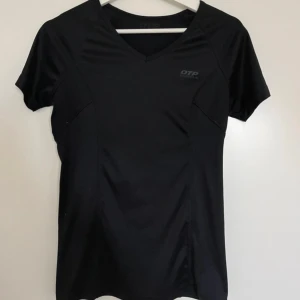 Svart träningst-shirt från OTP - Sportig svart t-shirt från OTP med v-ringad hals och korta ärmar. Tillverkad i lätt polyester som andas, perfekt för träning. En diskret reflexdetalj på ryggen för extra synlighet. Enkel och stilren design som funkar till gymmet eller löprundan.