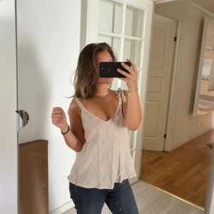 Beige linnetopp med knyt från Stajl - Säljer en superfin beige linnetopp från Stajl med v-ringad fram och bak. Toppen har knytband på axlarna och är tillverkad i mjukt linne. Perfekt för varma dagar och har en loose passform som ger en chill vibe. 100% äkta Linne material! 