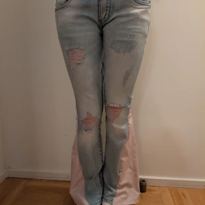 Ljusblå bootcut jeans med slitningar - Säljer ett par ljusblå och rosa bootcut jeans med slitna detaljer och hål på låren och knäna. Har då designat om dem till bootcut och sytt dem mer lågmidjade. Passar min syster som är 158