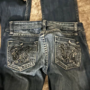 Mörkblå jeans med broderade bakfickor - Snygga mörkblå jeans med låg midja och raka ben. Bakfickorna har detaljerade broderier i svart och grått som ger en unik look. Jeansen har flera framfickor och klassisk jeanssöm. Perfekta för dig som vill sticka ut lite extra. Lågmidjade!!