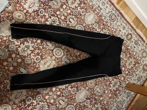 Svarta tights  - Svarta byxor med smal passform och orange kant längs benen. De har hög midja och är gjorda i ett stretchigt syntetmaterial. 