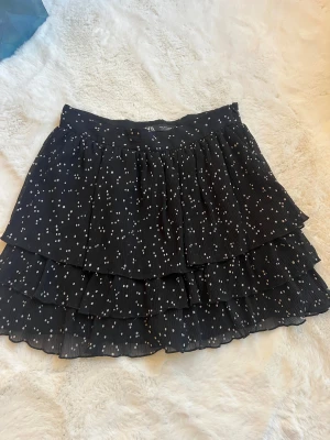 Svart prickig volangkjol från Zara - Supersöt svart kortkjol från Zara med vita prickar och flera lager volanger.