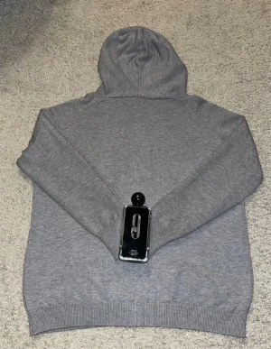 Grå hoodie med snörning - Mjuk och enkel grå hoodie med huva och snörning framtill. Tröjan har långa ärmar och ribbade muddar vid ärmslut och nederkant. Perfekt för chill dagar och passar till allt. Materialet känns som bomull eller polyester.