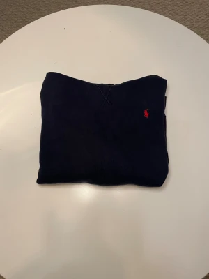 Mörkblå hoodie från Polo Ralph Lauren  - Snygg mörkblå hoodie från Polo Ralph Lauren i storlek XL/TG som passar till en kille på 160cm . Tröjan har huva, magficka och den klassiska röda broderade loggan på bröstet. Tillverkad i mjuk bomull, perfekt för chill dagar. Enkel och stilren design som funkar till jeans eller joggers.