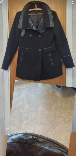 Svart rock med skinnkrage - Snygg svart rock med dubbla knappar och detaljer i skinn på kragen och fickorna. Jackan har en klassisk form med lång ärm och stilrena linjer, perfekt för dig som gillar en lite mer dressad look. Skinninslagen ger en cool kontrast till det svarta tyget. Material på kragen har lossnat lite.