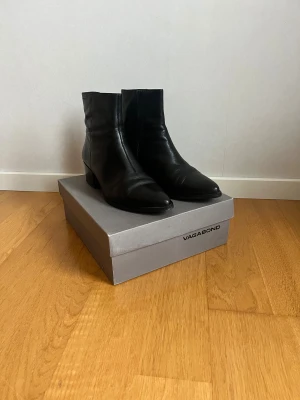 Svarta stövletter från Vagabond - Snygga svarta stövletter från Vagabond med spetsig tå och låg klack. Skorna är tillverkade i slätt skinn och har dragkedja på insidan för enkel på- och avtagning. Perfekt för dig som gillar stilrena boots med modern siluett.