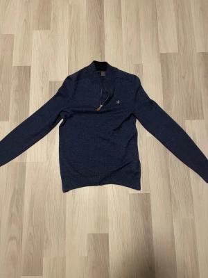 Marinblå stickad half zip-tröja  - Snygg marinblå stickad tröja från Morris med half zip och liten broderad logga på bröstet. Tröjan har lång ärm, ribbade muddar och en klassisk ståkrage. Perfekt för dig som gillar stilrena och bekväma plagg med lite extra detalj. Nypris cirka 1500 