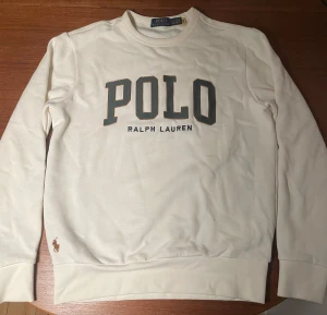 Vit sweatshirt från Polo Ralph Lauren - Vit sweatshirt från Polo Ralph Lauren med stor broderad POLO-logga på bröstet och liten brunt broderad häst vid nederkanten. Tröjan har rund hals, långa ärmar och är gjord i mjuk bomull. Den är använd ett fåtal gånger där inget har hänt så skiljer säga 10/10 i skick! Perfekt för dig som gillar klassisk och clean stil.