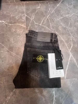 Stone island jeans - Snygga svarta jeans från Stone Island med klassisk patch med gul broderad kompass på bakfickan. Modellen heter TYPE RE-T och har en cool tvättad look. Jeansen har raka ben och är tillverkade i slitstarkt bomullsmaterial. Perfekt för dig som gillar streetwear och exklusiva detaljer. Grå-svart färg