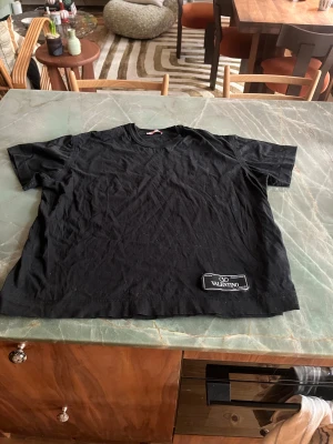 Svart Valentino t-shirt med patch - Svart t-shirt från Valentino med klassisk rund hals och korta ärmar. T-shirten är i mjuk bomull och har en snygg svart patch med Valentino-logga nedtill på framsidan. Stilren och enkel design som ändå sticker ut med logodetaljen.