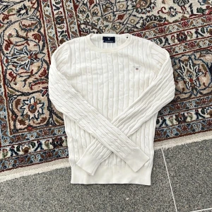 Vit kabelstickad tröja från Gant XS - Säljer en nästan helt ny vit kabelstickad tröja från Gant i stretchig bomull. Säljes då den var för liten på mig! Tröjan har en  klassisk rund halsringning, diskret Gant-logga på bröstet och ribbade muddar vid ärmslut och nederkant. Riktigt fin tröja för ett riktigt bra pris!😁