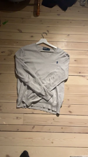 Ljusgrå v-ringad tröja från Polo Ralph Lauren - Säljer en stilren ljusgrå v-ringad tröja från Polo Ralph Lauren med den klassiska blå loggan broderad på bröstet. Tröjan är i mjuk bomull och har långa ärmar. Perfekt för lager-på-lager och enkel att matcha. Storlek S. Hör av dig vid frågor och funderingar!    Byten kan vara intressant 