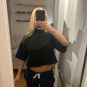 Svart croppad polotopp med kort ärm - Säljer en svart croppad polotopp med korta, vida ärmar och hög krage. Toppen är stickad och har en loose passform som ger en chill vibe. Perfekt att styla med höga jeans eller kjol för en trendig look.