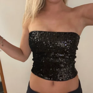 Svart paljett tubtopp - Säljer en svart tubtopp med glittriga paljetter som ger en riktigt snygg och festlig vibe. Toppen är axelbandslös och har en tight passform som sitter perfekt. Perfekt för dig som vill sticka ut och glänsa på nästa event!