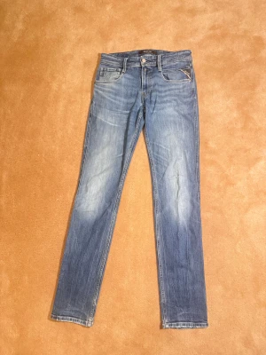  Replay jeans  - Snygga blå jeans från Replay med klassisk femficksdesign och ljusa slitningar. Modellen har rak passform och normal midja, med Replay-logga på bakfickan och läderpatch i midjan. Perfekt för dig som gillar stilrena och tidlösa jeans. Skick-9-10. Nypris 1299kr. Mitt pris 399kr