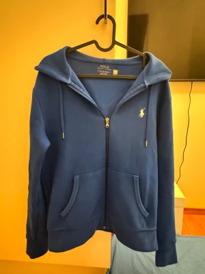  Polo Ralph Lauren zip hoodie - Snygg blå hoodie från Polo Ralph Lauren med dragkedja och huva. Tröjan har långa ärmar, fickor framtill och den klassiska Polo-loggan broderad på bröstet. Materialet är mjuk bomull blandat med polyester för extra komfort. Självklart äkta, nypris är 2300kr, pris kan justeras något vid en snabb affär