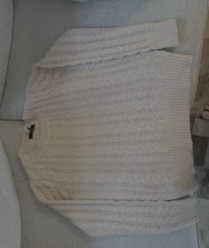 Beige stickad kabeltröja - Säljer en beige stickad tröja från H&M med klassiskt kabelstickat mönster. Tröjan har rund hals och långa ärmar med ribbade muddar. Perfekt för dig som gillar en chill och snygg look under höst och vinter.