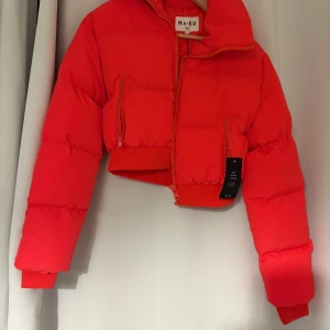 Röd croppad pufferjacka från NA-KD - Snygg croppad pufferjacka från NA-KD i starkt röd färg. Jackan har långa ärmar, hög krage och två dragkedjefickor framtill. Tillverkad i polyester och har en oversized vibe med breda muddar och quiltad look.