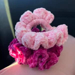 Rosa fluffiga egenvirkade hårsnoddar - Två supermjuka och fluffiga hårsnoddar virkade av mig. En ljusrosa och ett ceriserosa. Båda har en rund, bullig form med tydlig textur som ger en söt och lekfull look. Perfekt för att ge frisyren extra volym och färg. Säljes tillsammans!