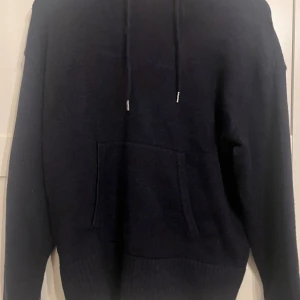 Mörkblå stickad hoodie med huva från Zara - Mysig mörkblå stickad hoodie med huva och dragsnören. Tröjan har en stor känguruficka framtill och ribbade muddar vid ärmslut och nederkant. Perfekt för kyliga dagar när du vill vara både bekväm och snygg.