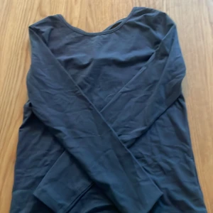 Svart långärmad topp från Lindex - Grå långärmad topp från Lindex med snygg detalj i form av korsade band på ryggen. Enkel och stilren design som passar perfekt till jeans eller kjol. Tillverkad i mjukt och stretchigt material för en bekväm känsla hela dagen.