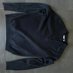 Mörkblå stickad tröja med half zip - Mörkblå stickad tröja från dobber i storlek M. Tröjan har en klassisk krage och en snygg half zip-dragkedja framtill. Perfekt för lager-på-lager och passar till både jeans och chinos. Långärmad och mjuk i materialet. Aldrig använd. Ny pris 750kr