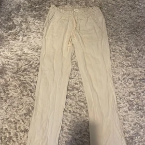 Beiga linnebyxor från Roxy med snörning - Snygga beiga linnebyxor från Roxy med elastisk midja och snörning framtill. Byxorna har raka ben, sidfickor och bakfickor med broderad logga. Perfekta för en chill och avslappnad stil under varmare dagar. 110kr+frakt