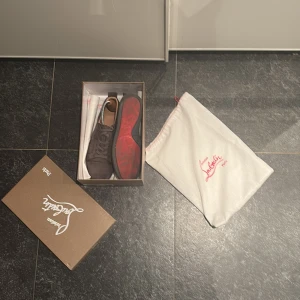 Christian Louboutin mocka sneakers - Säljer ett par mörkbruna sneakers från Christian Louboutin i lyxig mocka med klassisk röd sula. Skorna har rund tå, snörning och diskret branding. Kommer med originalkartong och dustbag. Perfekta för dig som vill ha något exklusivt och stilrent.