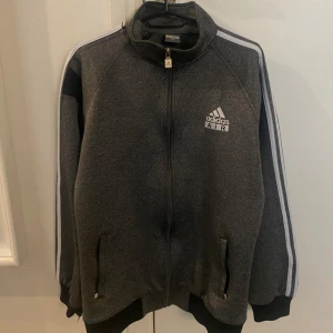 Vintage grå Adidas track jacket 2XL - Snygg vintage grå track jacket från Adidas med vita ränder längs ärmarna och svart detalj vid axlarna. Jackan har dragkedja framtill, ståkrage och två fickor. Adidas AIR-logga på bröstet och ryggen. Perfekt för en sportig och avslappnad stil. Storlek 2XL ( jag är storlek S/M )