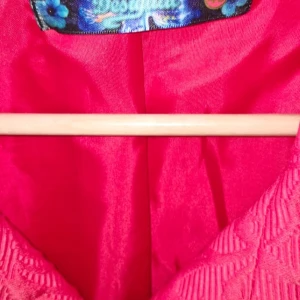 Mönstrad rosa kappa från Desigual - Unik rosa kappa från Desigual med svart mönster och snygga knappar framtill. Jackan har en klassisk krage och är helfodrad med ett glansigt tyg. Materialet är strukturerat och ger en cool känsla. Perfekt statement-plagg för dig som vill sticka ut.