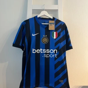 Inter Milan matchtröja Nike blå/svart - Inter Milan fotbollströja från Nike med klassiska blå och svarta ränder, klubbmärke och två stjärnor på bröstet. V-ringad hals, broderad Nike-logga och sponsortryck. Tillverkad i lätt och ventilerande polyester, perfekt för match eller träning.