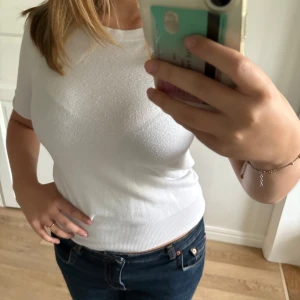 Vit ribbad topp med kort ärm - Säljer en stilren vit topp med korta ärmar och ribbad nederkant, krage och längst ner på ärmarna. Den är lite nopprig som synd på bilden men inget som man riktigt tänker på!