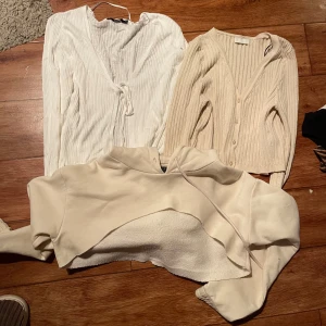 Tre trendiga tröjor i neutrala toner - Säljer tre snygga tröjor: en ribbad vit omlottkofta med knyt, en beige ribbad kofta med knappar och en croppad hoodie i offwhite med huva. Perfekta basplagg i garderoben och superlätta att matcha till olika outfits. Blandade storlekar L-XL.
