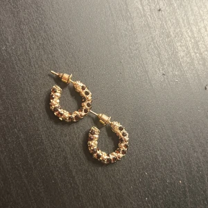 Glittriga guldiga hoops örhängen - Säljer ett par örhängen i guld med glittriga stenar i mörkröd. Naglacket är bara för att se storleken på de🤗aldrig använda och de kommer från ur o Penn!