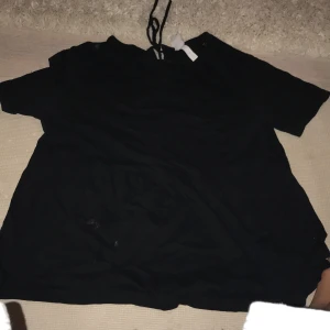 Svart blus med knyt i ryggen  - En svart blus med korta ärmar och knytband i ryggen . Blusen har en lätt v-ringning framtill och ett löst fall nedtill. Perfekt för dig som gillar en enkel men ändå snygg look.